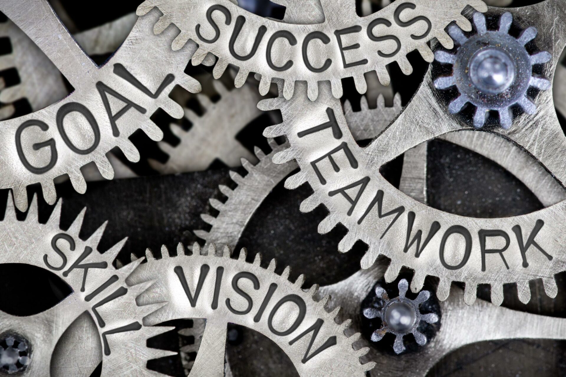 Macro photo of tooth wheels with TEAMWORK, SUCCESS, GOAL, VISION and SKILL words imprinted on metal surface